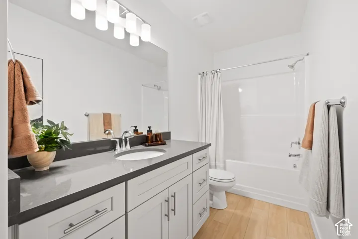 Spacious basement bathroom featuring a single vanity with a gray countertop, white shaker-style cabinetry, and wood-finish flooring