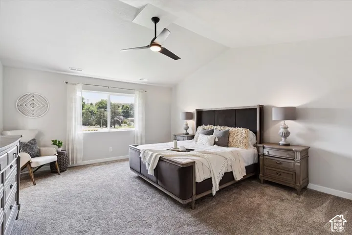 Primary bedroom featuring vaulted ceilings with a ceiling fan, large window, and carpeted flooring