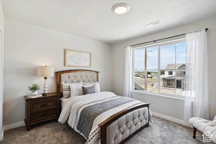 Spacious bedroom featuring a large window, neutral wall paint, and gray carpet flooring