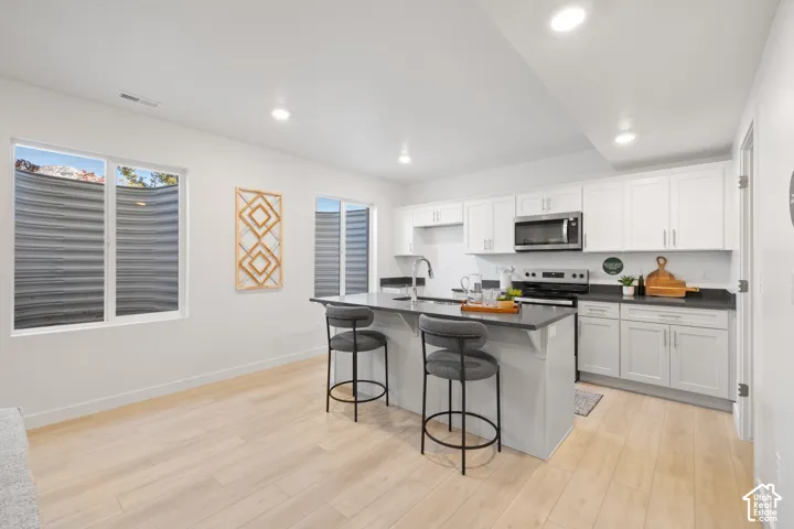 ADU kitchen featuring white shaker cabinetry, dark countertops, a stainless steel appliance suite, an island with seating, and light wood-finish flooring