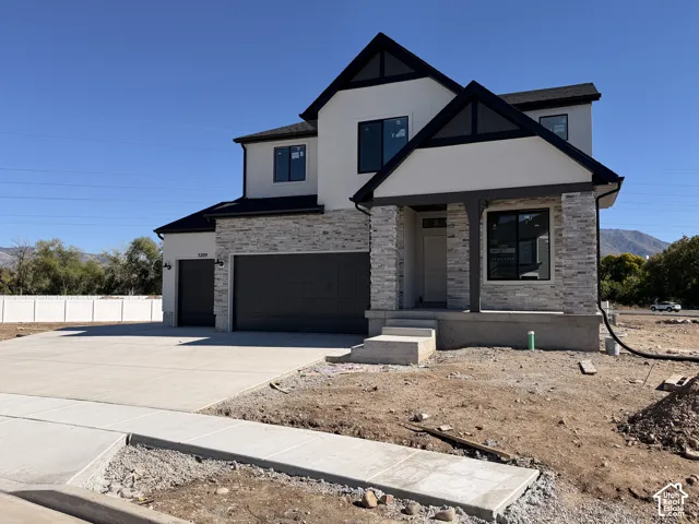 Two-story exterior featuring a stone veneer facade, stucco siding, a multi-gabled roofline, and a three-car garage