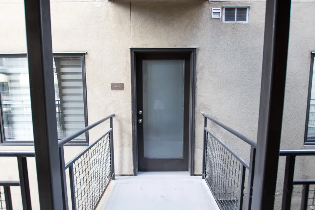 Entryway featuring a frosted glass door, stucco exterior, and black metal railings with mesh infill