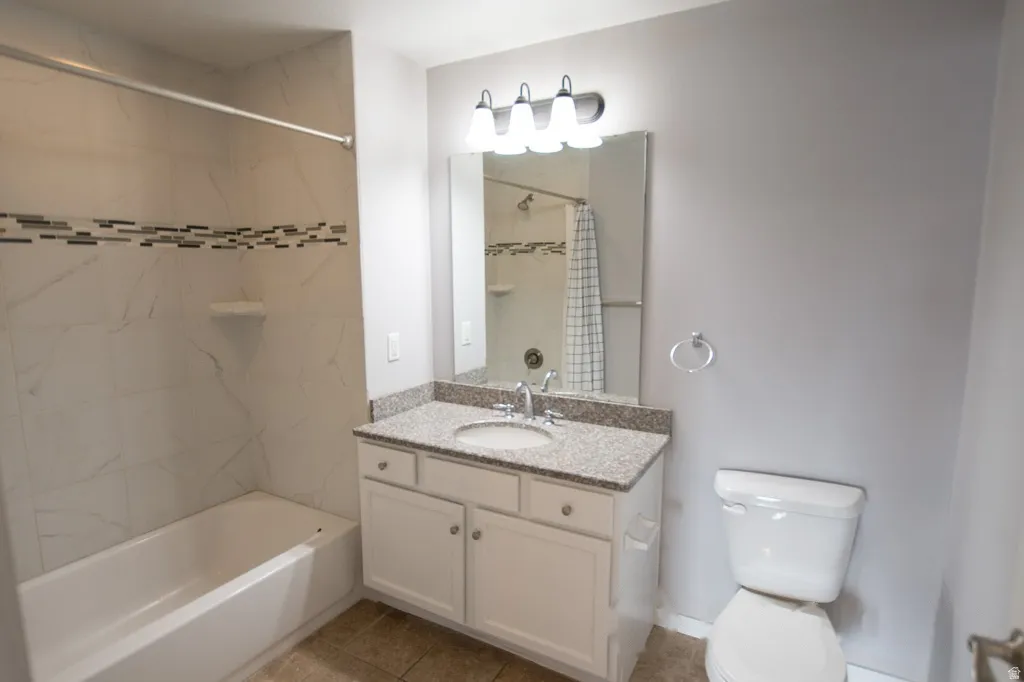 Bathroom featuring a tub/shower combination with tile surround and decorative accent band, a white vanity with a granite countertop and integrated sink, a wall-mounted mirror, and a modern light fixture