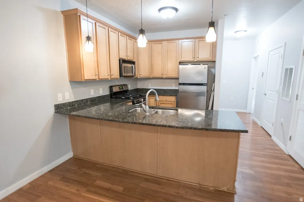 Kitchen featuring a peninsula with a dark countertop, stainless steel appliances, wood-finish flooring, and pendant lighting