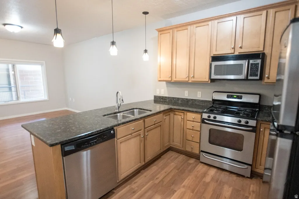 Kitchen featuring light wood cabinetry, stainless steel appliances, dark stone countertops, and wood-finish flooring