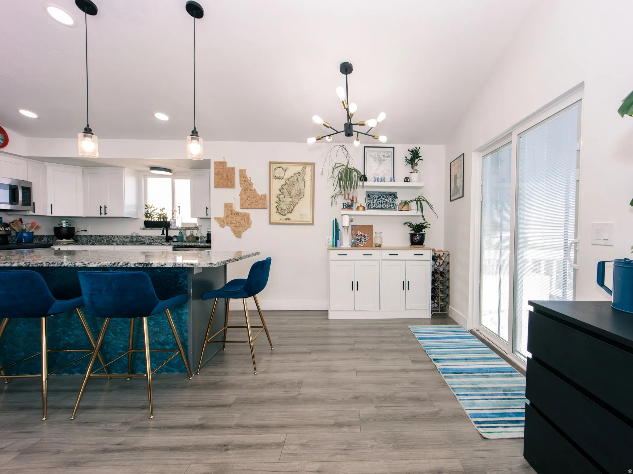 Open concept living area featuring wood-finish flooring, a kitchen island with pendant lighting, white cabinetry, and a sliding glass door