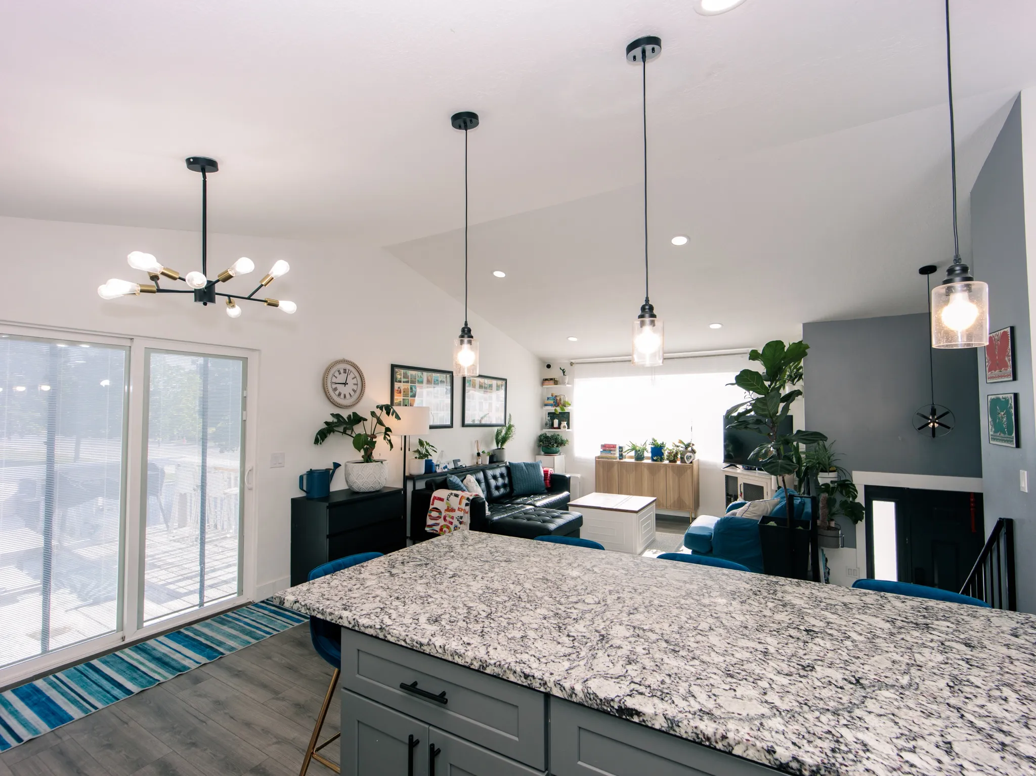 Open-concept living space featuring a spacious kitchen island with a light-toned countertop, pendant lighting, sliding glass doors, and wood-finish flooring