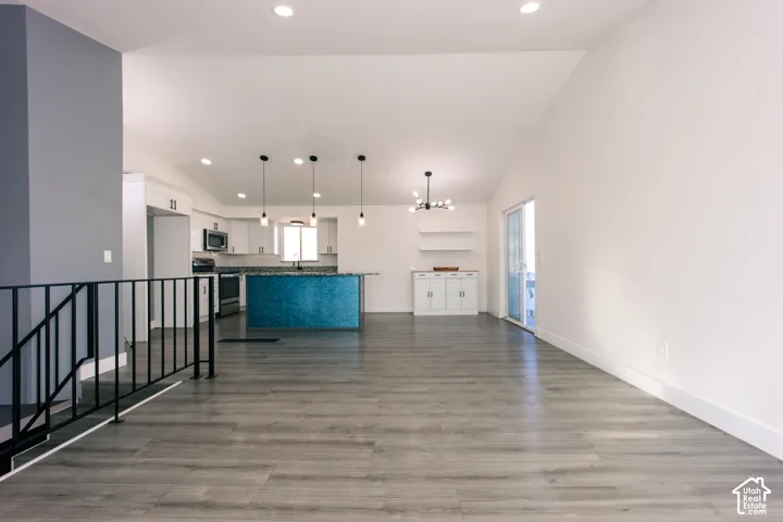 Open-concept interior featuring vaulted ceilings, wood-finish flooring, recessed lighting, and a kitchen island with tiled surfacing