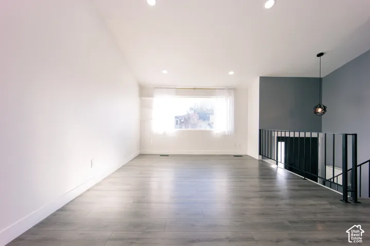 Open-concept space featuring wood-finish flooring, recessed lighting, matte black metal railing, and a distinctive orb-style pendant light