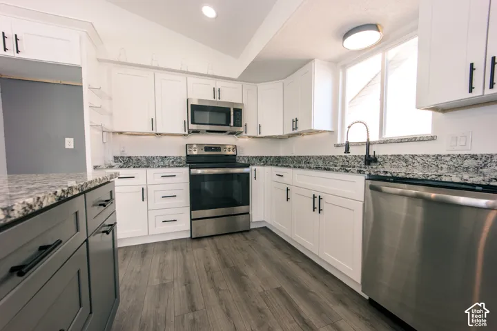 Kitchen featuring white shaker-style cabinetry with matte black hardware, stone-finish countertops, stainless steel appliances, and wood-finish flooring
