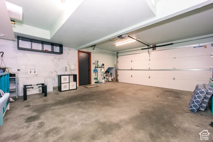 Attached garage featuring a concrete floor, stone-pattern wall detailing, built-in overhead storage shelving, and an automated sectional garage door