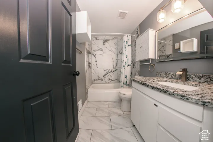 Bathroom featuring a vanity with stone-finish countertop, undermount sink, wall-mounted light fixture, large vanity mirror, and bathtub with floor-to-ceiling tile surround