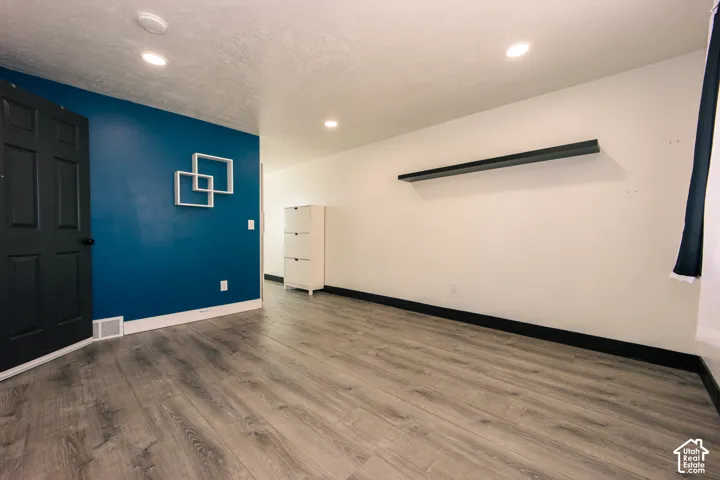 Interior room featuring wood-finish flooring, recessed lighting, a contrast-painted accent wall, a built-in wall shelf, and a multi-panel door