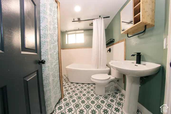 Bathroom featuring patterned floor tile, pedestal sink with matte black faucet, soaking tub, wall-mounted medicine cabinet, and dark-toned door