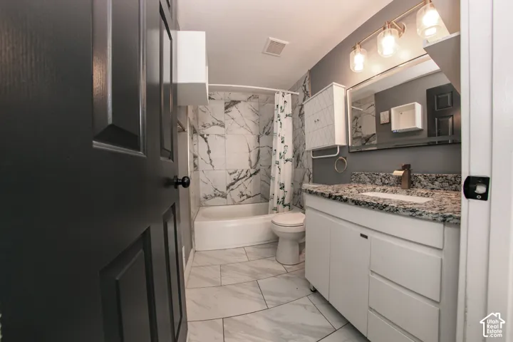 Bathroom featuring a stone-pattern vanity countertop, large-format tile flooring, shower walls with tile surround, a built-in wall cabinet, and a multi-light fixture
