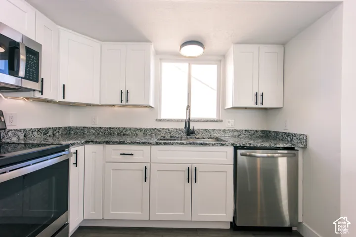 Kitchen featuring white shaker-style cabinetry, speckled stone-finish countertops, stainless steel appliances, a pull-down kitchen faucet, and under-cabinet lighting