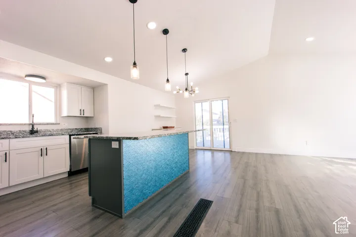 Kitchen featuring white cabinetry, stone-finish countertops, stainless steel appliances, a center island with decorative blue tile detailing, and wood-finish flooring under vaulted ceilings