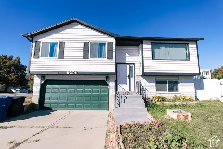 Split-level exterior featuring white horizontal siding, a painted brick facade, a two-car garage with a green sectional door, and a concrete driveway