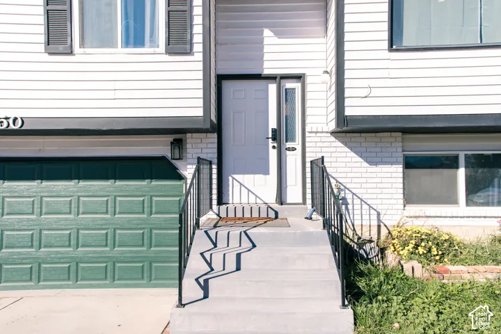 Exterior facade featuring white horizontal siding, a painted brick lower level, a multi-panel front door with glass sidelight, and an attached garage with a green sectional door