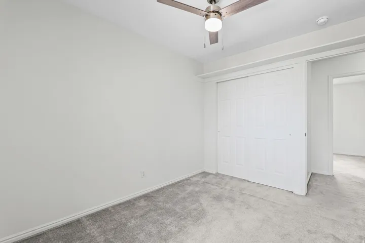 Interior room featuring a ceiling fan with integrated lighting, neutral gray carpeting, and white baseboards