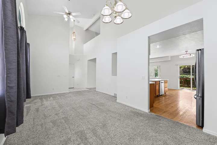 Spacious living area featuring vaulted ceilings, ceiling fan, and carpet flooring