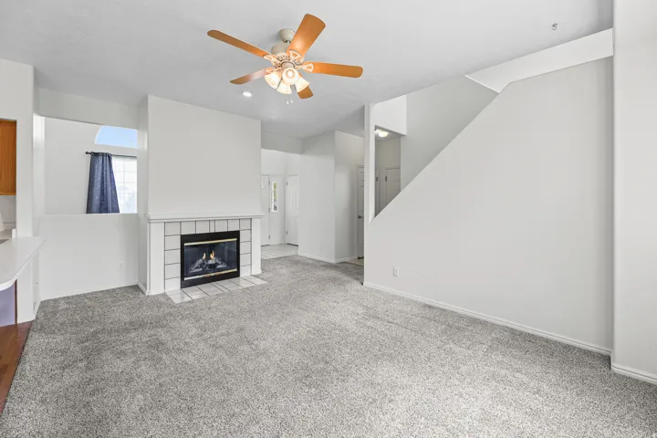 Living area featuring a fireplace with white tile surround, ceiling fan, carpet flooring, and a half-wall partition