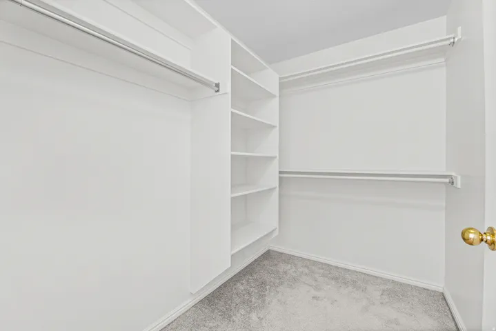 Walk-in closet featuring built-in shelving, two clothing rods, white walls, and gray carpet flooring
