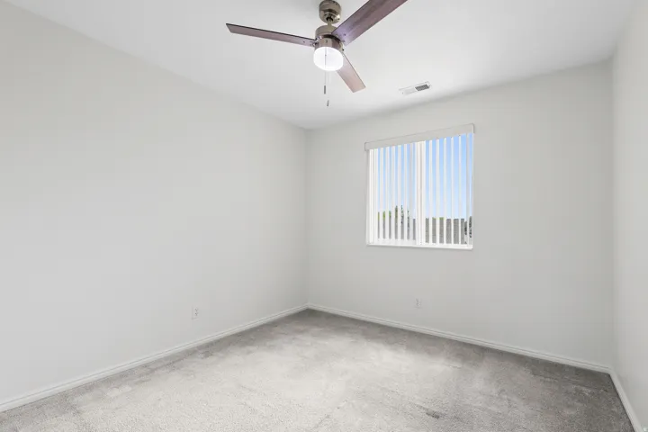 Room featuring neutral carpeting, white walls, a single window with vertical blinds, and a ceiling fan with light fixture