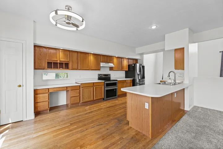 Kitchen featuring wood-finish flooring, wood cabinetry, built-in double oven, and a kitchen island with a sink