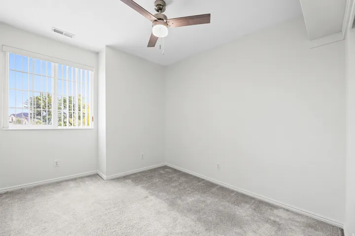 Bright room with a large window, vertical blinds, a ceiling fan with integrated lighting, and gray carpeting