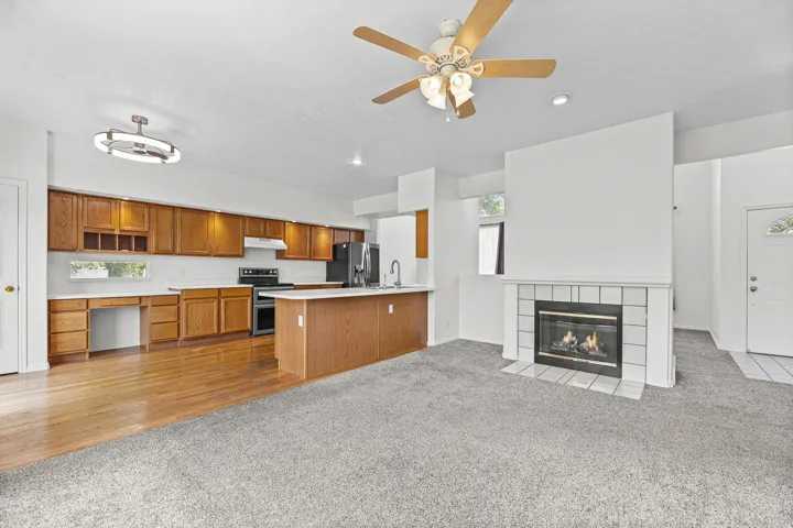 Living area featuring a fireplace with white tiled surround, carpet flooring, and a ceiling fan