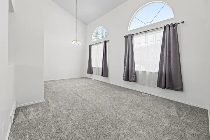 Spacious room featuring vaulted ceilings, a suspended ceiling light fixture, and light gray carpeting