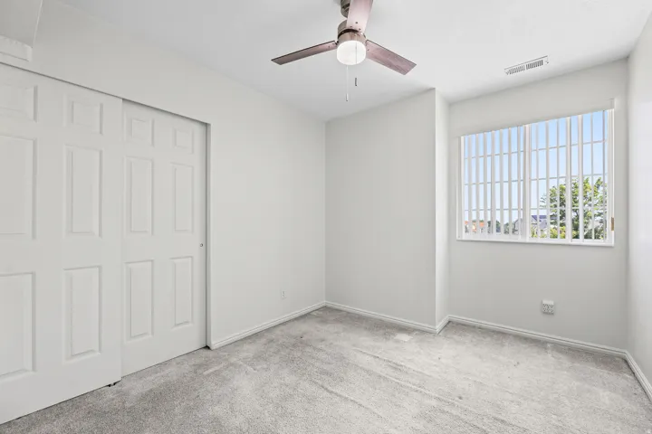 Light-filled room featuring a large window with vertical blinds, neutral carpeting, and a ceiling fan