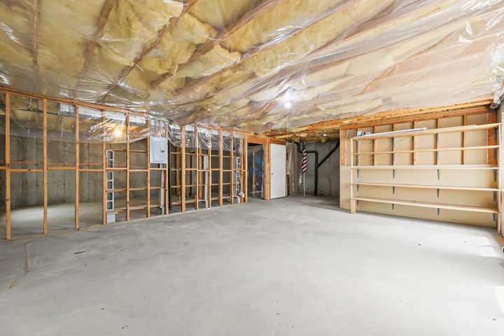 Unfinished basement with concrete flooring, exposed ceiling insulation, wood framing, and built-in shelving