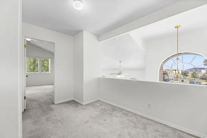 Loft area featuring a large arched window, vaulted ceilings, and light gray carpet flooring