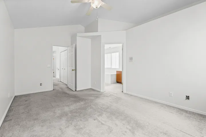 Carpeted bedroom featuring vaulted ceilings, a ceiling fan, and white walls