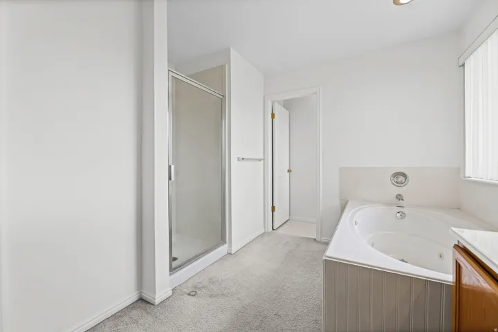White bathroom featuring a glass-enclosed shower, a jetted soaking tub with beadboard paneling, and neutral carpeting