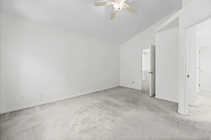 Spacious room featuring vaulted ceilings, light gray carpeting, and a ceiling fan with integrated lighting