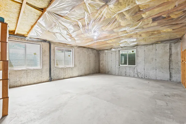 Unfinished basement featuring concrete walls, exposed ceiling joists with insulation, and multiple windows