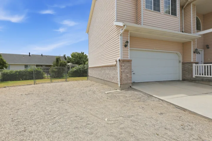 Exterior featuring light-colored siding, an attached garage, a concrete driveway, and a chain-link fence