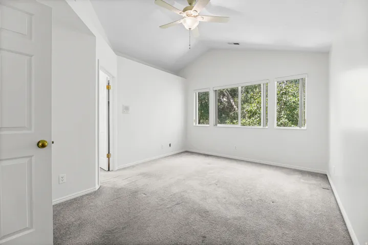 Spacious room featuring vaulted ceilings, a ceiling fan, and multiple windows providing ambient light