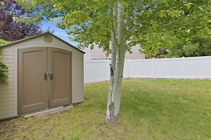 Backyard featuring a tan storage shed, mature tree, and a white privacy fence