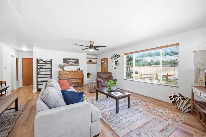 Open-concept living space featuring wood-finish flooring, a contemporary ceiling fan, and a large window with horizontal blinds