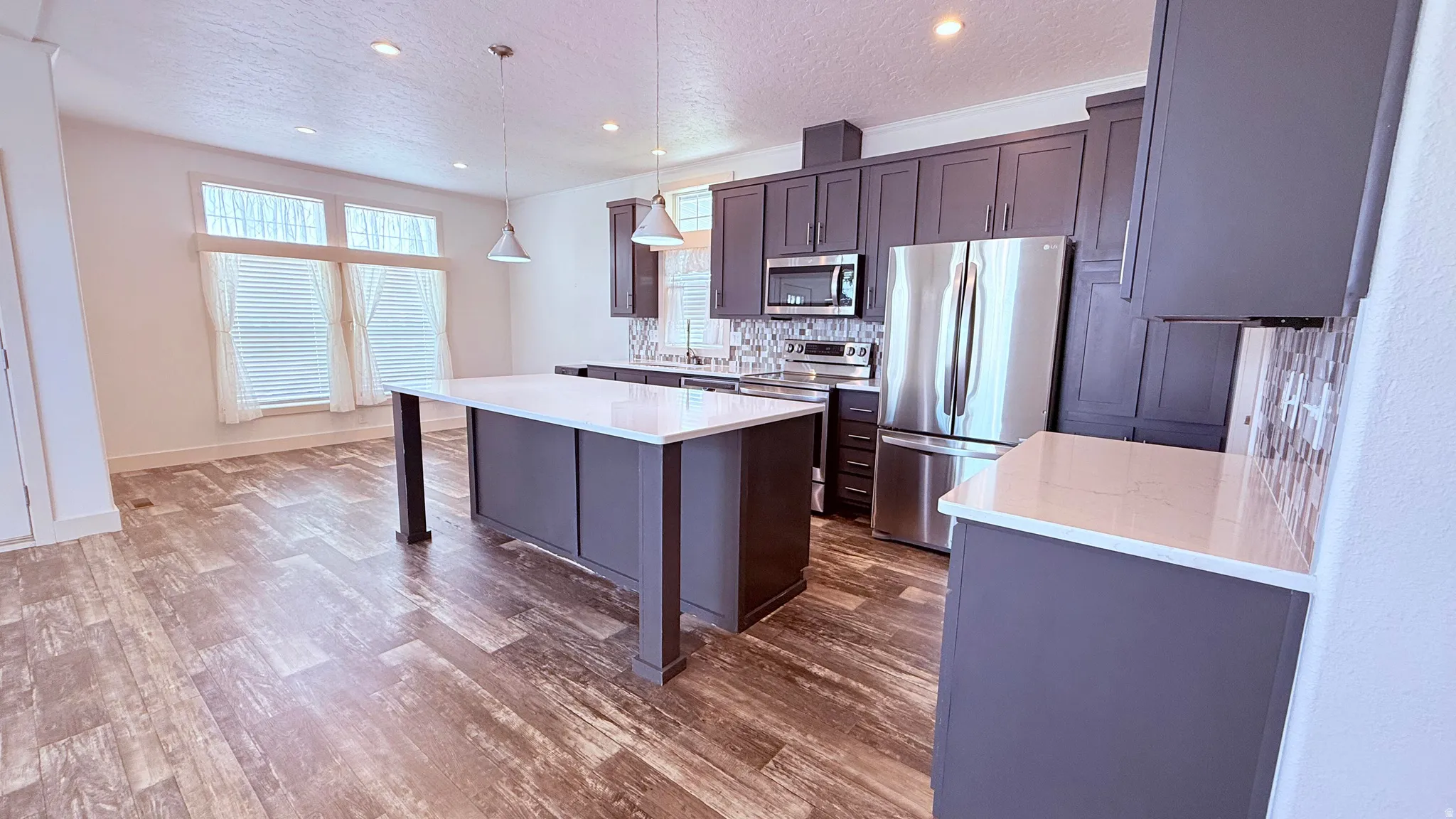 Kitchen featuring a large central island with a white countertop, gray cabinetry, and stainless steel appliances.