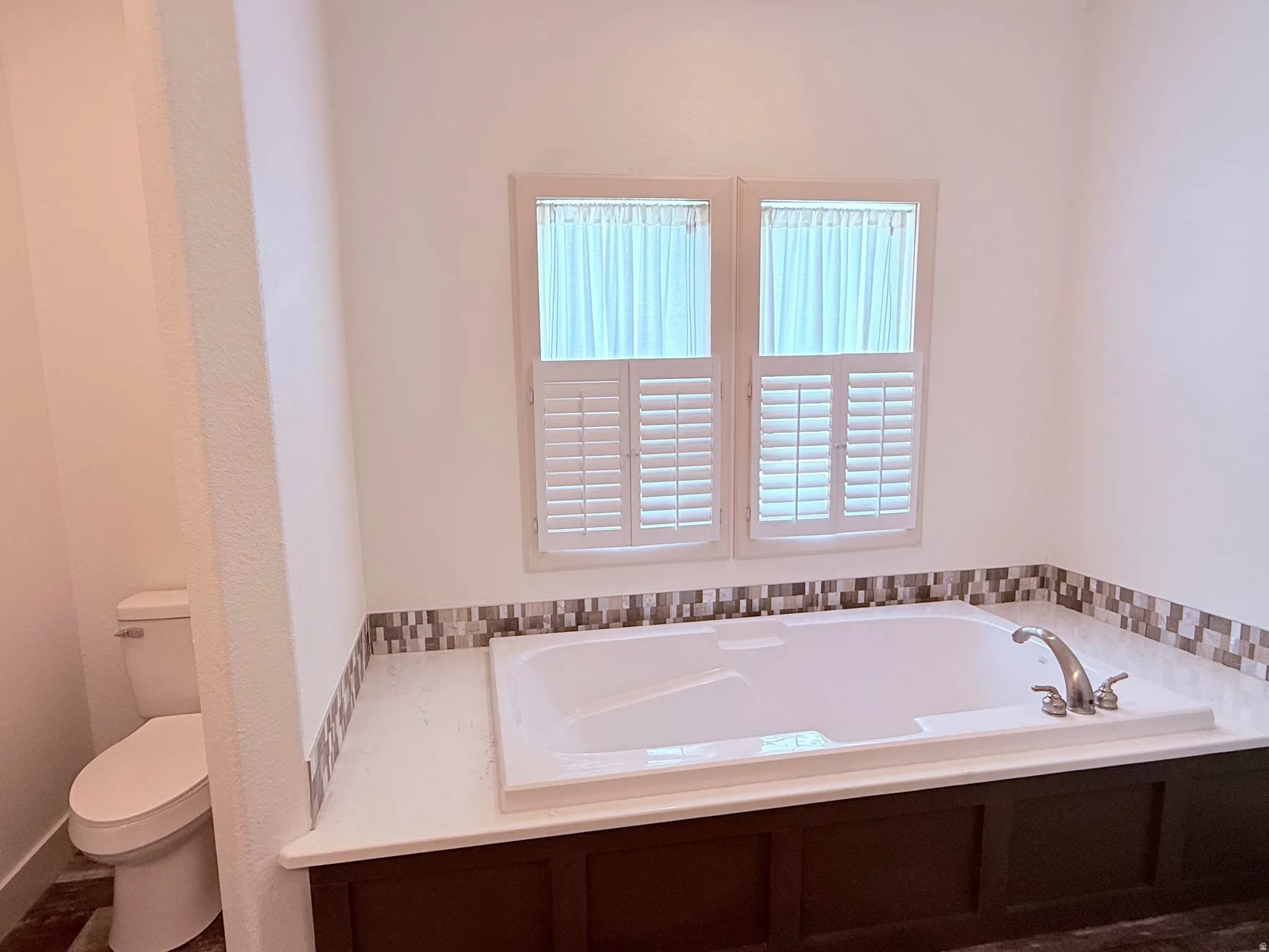 Built-in soaking tub with deck-mounted faucet and mosaic tile surround in Primary Bathroom