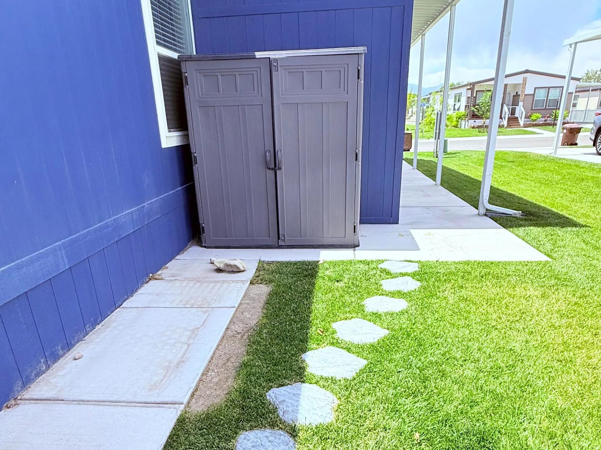 Included shed, vibrant blue exterior siding with white trim, featuring a side walkway with stepping stones and a covered patio area