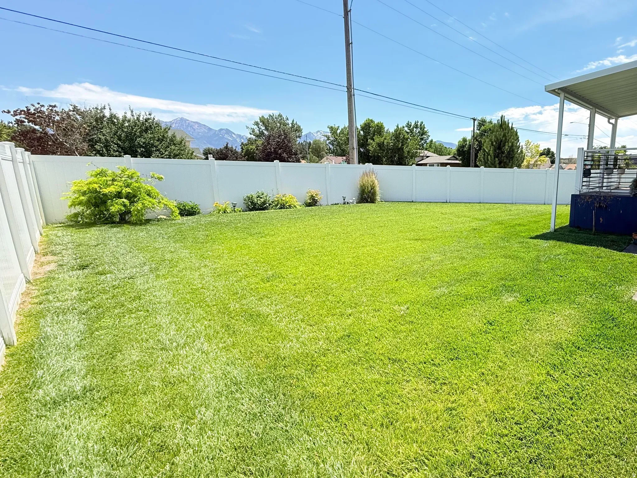 Expansive backyard featuring a green lawn, white vinyl fencing, and a covered patio deck