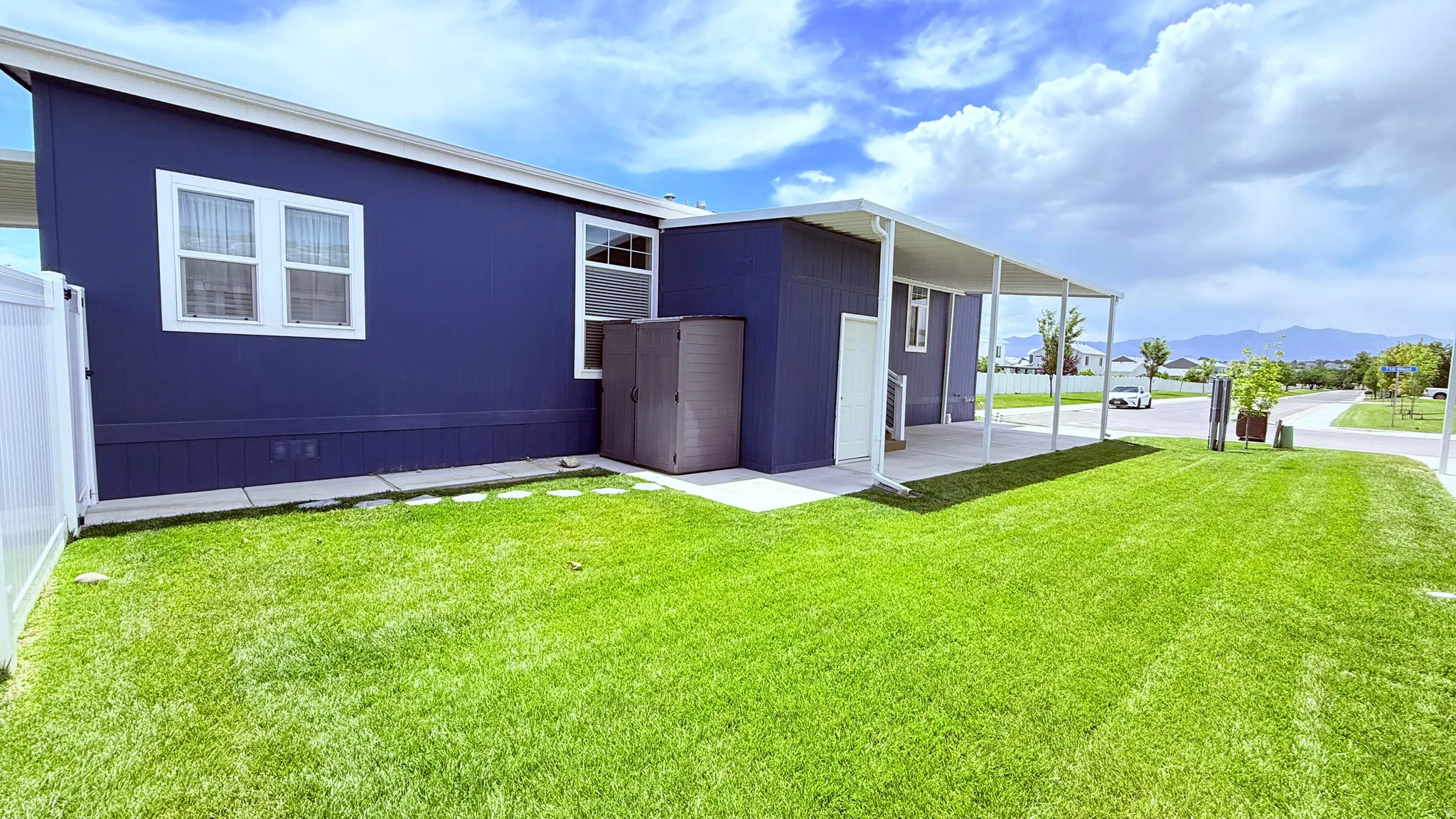 Included shed, expansive green lawn bordering the property, featuring a white fence and concrete patio with an extended white awning