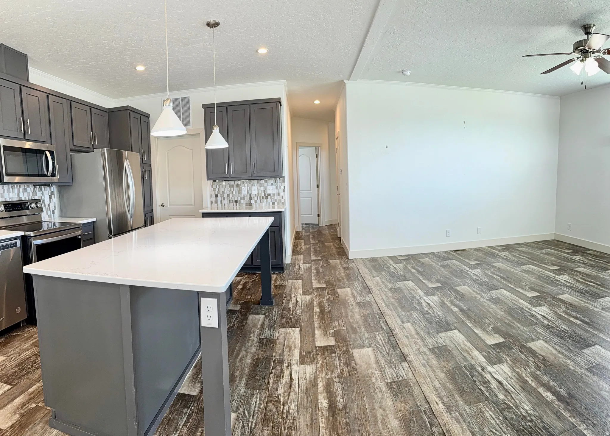 Modern kitchen featuring a large island with a light-toned countertop, gray shaker-style cabinetry, stainless steel appliances, and a mosaic tile backsplash
