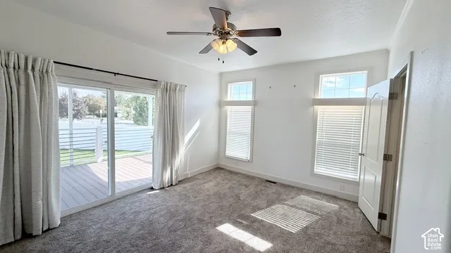 Sliding glass door leading to an outdoor deck, two windows with horizontal blinds, overhead ceiling fan with lighting, carpeted flooring, and a white interior door
